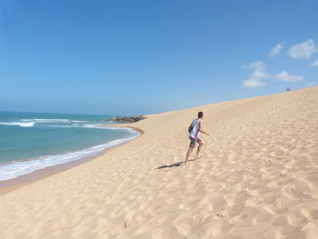 Man walking on sand dune at beach against sky