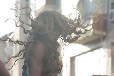 Woman tossing curly hair while standing in city