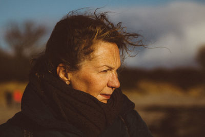 Mature woman wearing warm clothing looking away while standing against cloudy sky