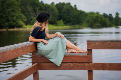 Woman wearing skirt looking at lake while sitting on railing