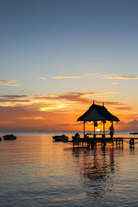 Silhouette swimming pool by sea against sky during sunset