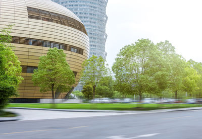 Trees by modern buildings against sky