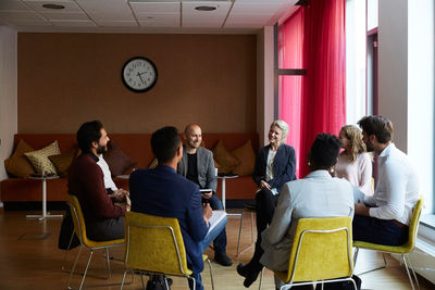 Smiling male and female entrepreneurs sitting in circle during office workshop