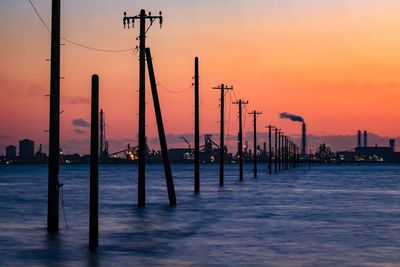 Silhouette of wooden post in sea against sky during sunset