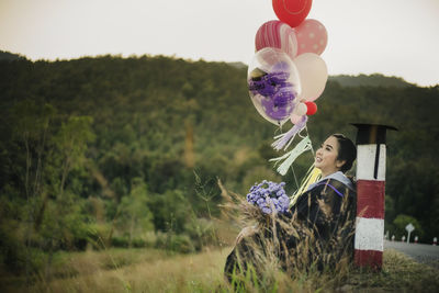 Side view of woman sitting with helium balloons against mountains