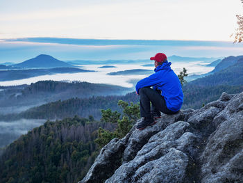 Rear view of man sitting on rock against mountains