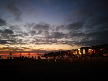 Illuminated buildings by sea against sky at sunset