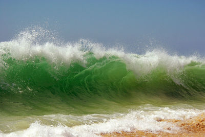 Sea waves splashing on shore against sky