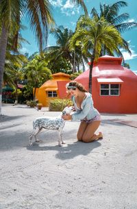 Side view of woman sitting on beach with dog and colorful homes in the background 