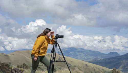 Latin american woman with her camera and tripod taking photos of landscapes on the top of a mountain