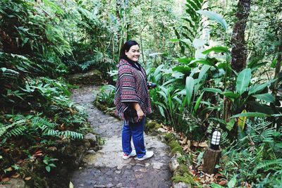 Full length portrait of young woman standing against plants