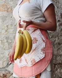 Midsection of woman holding bananas while standing against wall