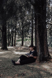 Side view of woman sitting on tree trunk in forest