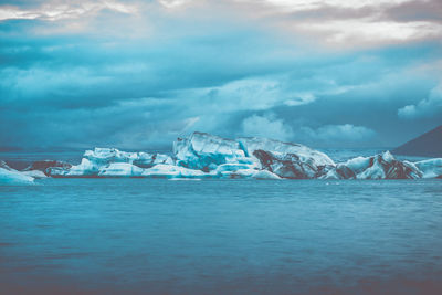 Scenic view of glaciers in sea against cloudy sky