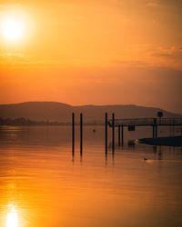 Silhouette wooden posts in lake against orange sky