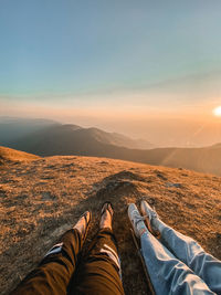 Low section of people sitting on mountain against sky during sunset