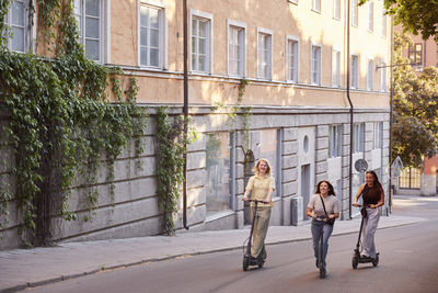 Young female friends spending time together outdoors riding electric scooters