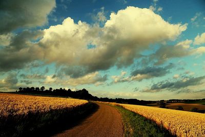 Road passing through field against cloudy sky