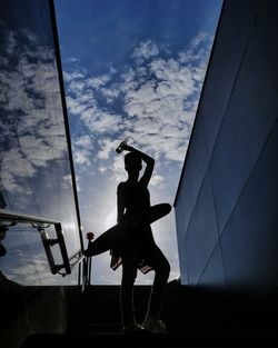 Low angle view of silhouette woman holding skateboard while standing against sky