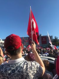 Group of people against red flag against clear sky