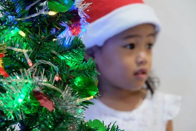Cute girl looking away by christmas tree at home