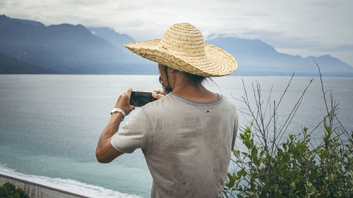 Midsection of man photographing by sea against mountain