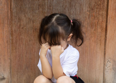 Girl crying while sitting against wooden door