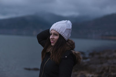 Thoughtful beautiful woman standing by lake during winter