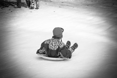 Rear view of boy tobogganing on snow