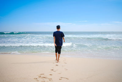 Rear view of man on beach against sky