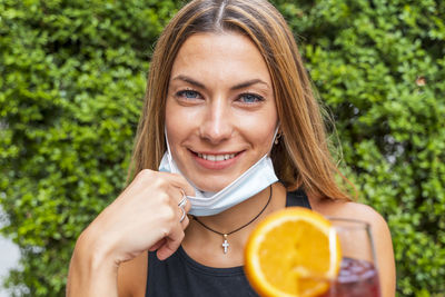 Portrait of smiling young woman holding drink against plant