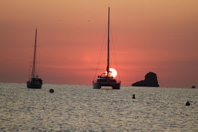 Sailboats in sea against sky during sunset