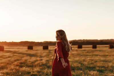 Young happy blonde in a red dress runs into a field at sunset.