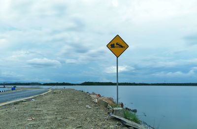 Road sign by river against sky