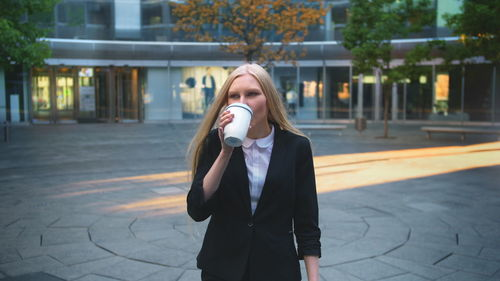 Young businesswoman drinking coffee while standing outdoors