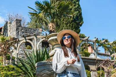 Front view of attractive young woman in spring outfit standing in beautiful park.