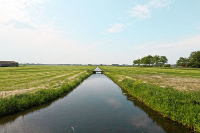 Scenic view of canal amidst field against sky