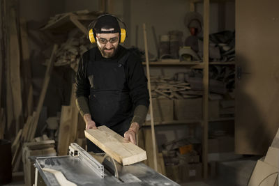 Carpenter sawing plank on circular saw at workshop