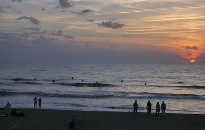 Silhouette people on beach against sky during sunset