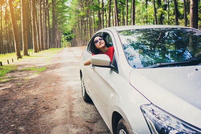 Smiling woman in car against trees in forest