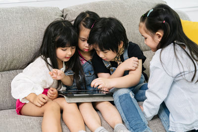 Friends using digital tablet while sitting on sofa