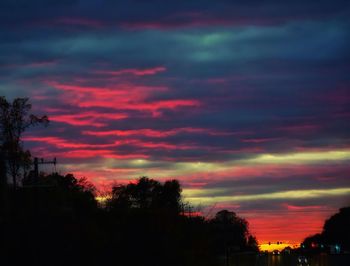 Silhouette trees against dramatic sky at sunset