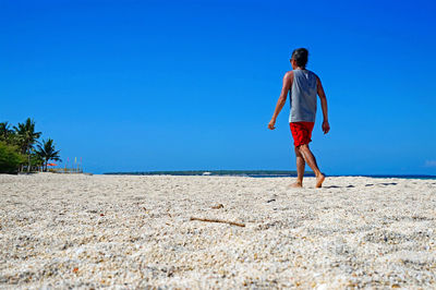 Rear view of man walking at beach against clear blue sky