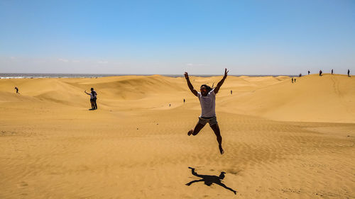 Man jumping on sand against sky at beach