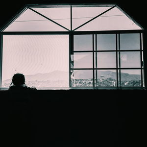 Rear view of silhouette man looking through window