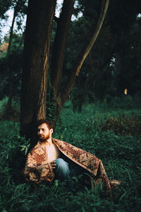 Portrait of young woman sitting on tree trunk in forest