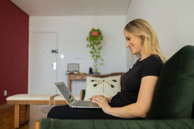 Woman working at home from couch with laptop on her lap. home office concept. gray notebook