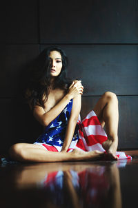 Portrait of woman with american flag sitting against wall