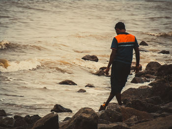 Rear view of man on rock at beach during sunset