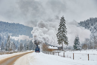 Snow covered road against sky featuring a steam train